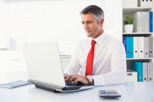 Cheerful businessman typing on laptop in his office